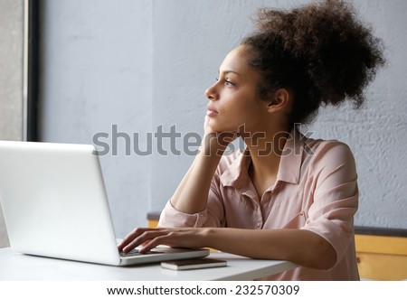 Close up portrait of a young african american woman looking out window when working on laptop Royalty-Free Stock Photo #232570309