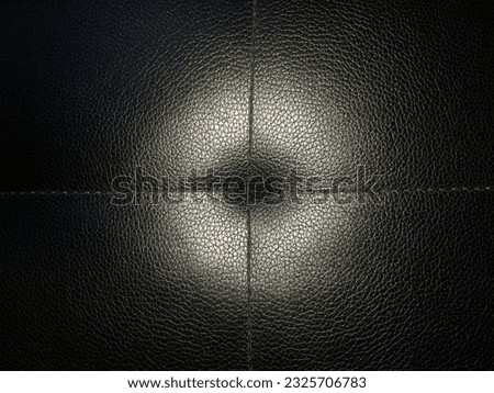 Black imitation leather with a small mesh print and two perpendicularly intersecting seams on the back of the armchair with a glow from a flash (macro, top view, texture, flash photo).

