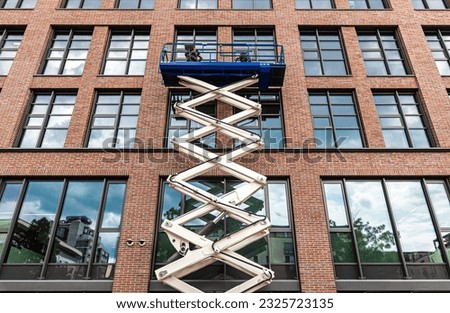 maintenance workers are repairing a modern building facade from an elevating scissor lift aerial work platform Royalty-Free Stock Photo #2325723135