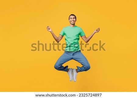Full body young man of African American ethnicity he wears casual clothes green t-shirt hat jump high spread hands in yoga om aum gesture relax meditate, calm down isolated on plain yellow background