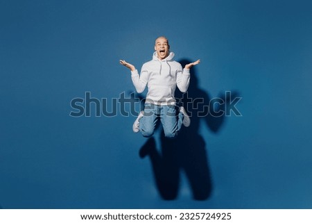 Full body overjoyed excited young dyed blond man of African American ethnicity wears white hoody jump high look camera spread hands isolated on plain dark royal navy blue background studio portrait