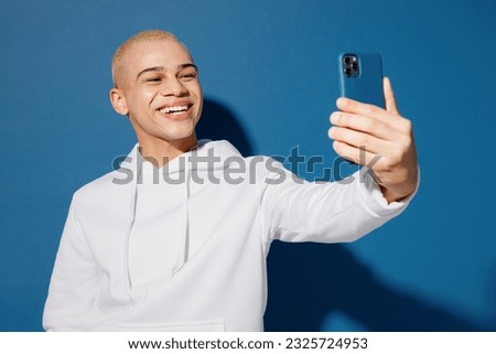 Young dyed blond man of African American ethnicity wear white hoody do selfie shot on mobile cell phone post photo on social network isolated on plain dark royal navy blue background studio portrait