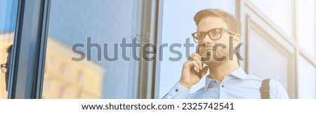 Young handsome caucasian businessman in blue shirt talking by phone while standing outdoors