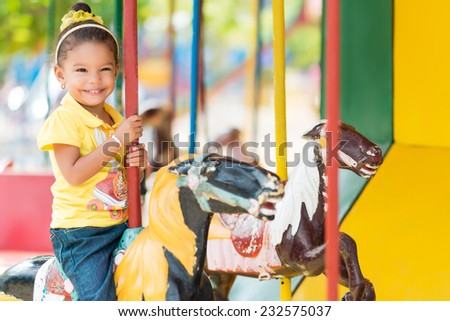 Cute small mixed race girl riding a colorful carousel