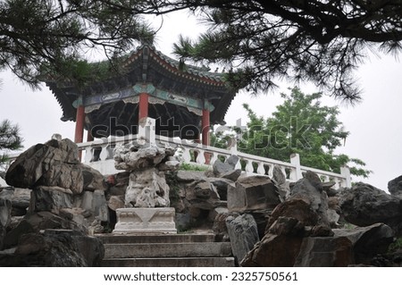 the photo was taken in a Chinese park with a gazebo on gazebos a beautiful Chinese ornament, in the background there is an oasis of trees and laid out stones, behind a path in the forest there 