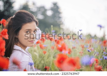 Side view of atractive brunette girl with hand in her hair posing in a red poppies field. Horizontally. 