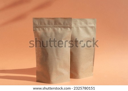 Two craft paper bags with a zipper in the background. The layout of the bag-bag on an orange background. Product Packaging Empty brown kraft paper packaging , product template copy space Royalty-Free Stock Photo #2325780151