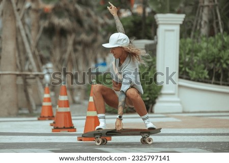 Image of athletic sporty woman 20s in tracksuits,  Freedom and happiness. Happy blond girl riding her board on an road with hurdle, laughing and smiling, skateboarding.