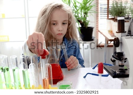 Primary school girl with long blonde hair doing chemistry science experiment in laboratory, cute scientist kid with colorful test tubes and lab equipment learning biologics and chemistry in classroom.