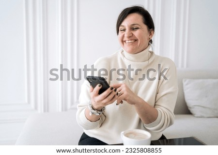 A cheerful woman drinks coffee from a cup, uses a phone and laptop, a freelancer works at home.
