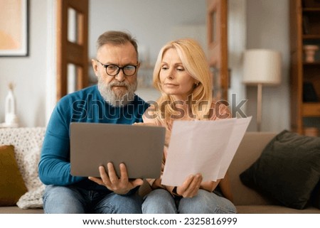 Household Papers Issue. Serious Mature Spouses With Laptop Doing Paperwork Together, Reading Bills And Correspondence Sitting On Couch At Modern Home Interior. Husband Wearing Glasses Royalty-Free Stock Photo #2325816999