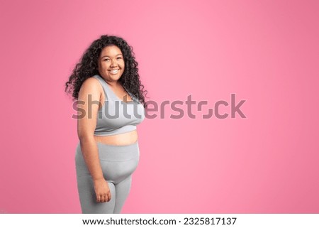 Portrait of body positive black lady in sports top bra and leggings posing and smiling at camera isolated on pink studio background, banner, free space