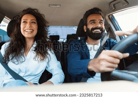 Front view portrait of happy middle eastern man driving modern luxury car and excited young woman sitting on the front passenger seat, looking on the road and smiling Royalty-Free Stock Photo #2325817213