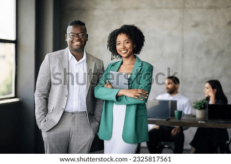 Business Career. Happy Couple Of Black Coworkers Posing At Modern Office Interior, Smiling At Camera. African American Businessman And Businesswoman Standing During Conference With Colleagues Royalty-Free Stock Photo #2325817561