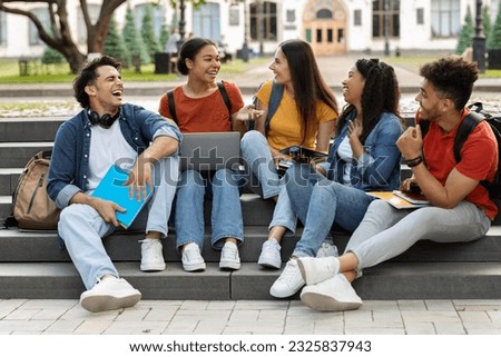 Campus Life. Cheerful multiethnic college students resting outdoors between classes, happy young men and women using laptop, chatting and laughing, sitting on stairs outside, free space Royalty-Free Stock Photo #2325837943