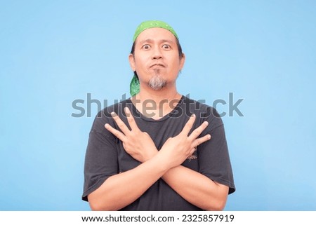 An intense middle-aged barista with wide eyes doing a W hand sign while his arms are crossed against his chest. Isolated on a blue background. Royalty-Free Stock Photo #2325857919