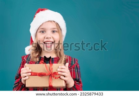 Little happy face girl in christmas hat holding box. Kid in santa's hat with gift in hands empty copy space. Child with holiday present.