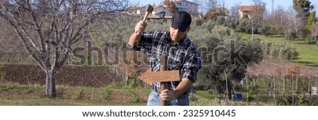 Image of a man driving a stake with an arrow into the ground with a hammer. Pole indicating the direction to take. Horizontal banner 
