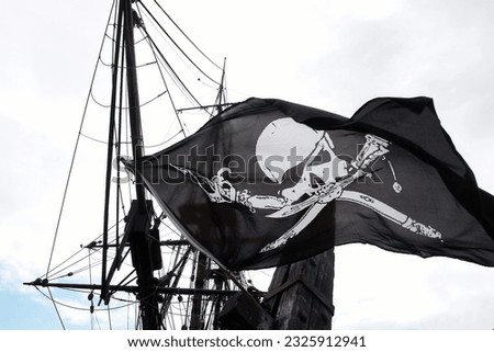 Detail of a real pirate flag with skull and shinbone called Jolly Roger fluttering in the wind among the rigging of an ancient wooden pirate ship