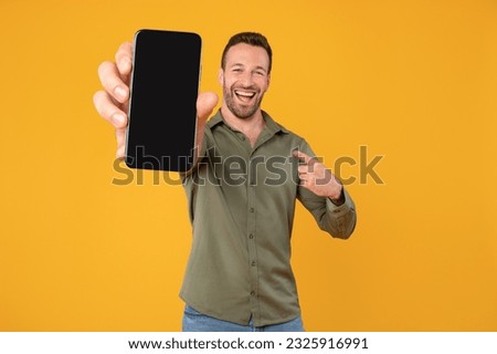 Excited caucasian man holding blank cellphone showing screen to camera pointing at it, recommending website or application, mockup banner