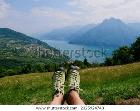 Woman's legs with green hiking boots, panoramic view of Lago d'Iseo seen from Fonteno - Riva di Solto Big Bench, Lombardy, Italy. High quality photo Royalty-Free Stock Photo #2325924743