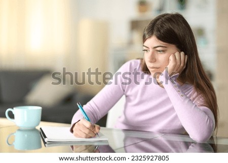 Distracted teen writing on notebook looking away at home Royalty-Free Stock Photo #2325927805