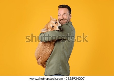 Happy european man holding and comforting cute corgi dog, smiling at camera, posing with pet over yellow studio background Royalty-Free Stock Photo #2325934007