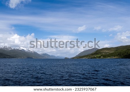 Norway's blue fjord with nearby mountains above which is a beautiful blue sky with puffy white clouds