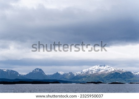 A Norwegian fjord on a harsh overcast day, with dark fjords in the distance and white snow capped with a dramatic sky.