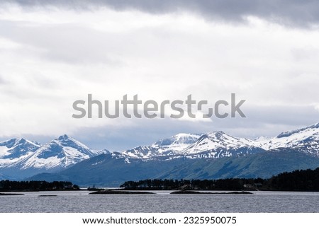 A Norwegian fjord on a harsh overcast day, with dark fjords in the distance and white snow capped with a dramatic sky.
