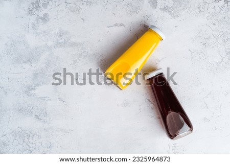 Bottles with yellow and red liquid halthy beverage on gray background. Orange and cherry juice