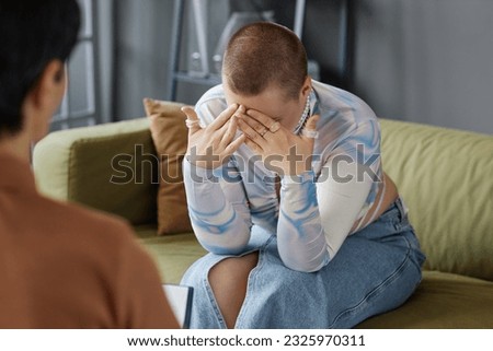 Young sad woman sitting on sofa and talking about her problems while visiting psychologist in office Royalty-Free Stock Photo #2325970311