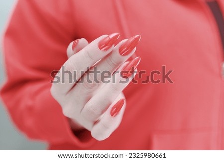 Female hand with long nails and a bright red manicure holds a bottle of nail polish