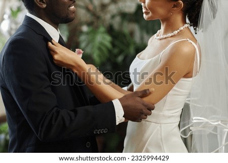 Side view closeup of black young couple getting married with bride adjusting jacket and boutonniere before wedding ceremony Royalty-Free Stock Photo #2325994429