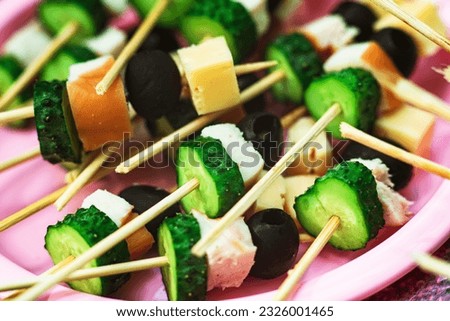 Picnic Canapes. Green cucumber, black olives, cheese on wooden sticks. Appetizing appetizers on a plate. Delicious and healthy snacks, macro