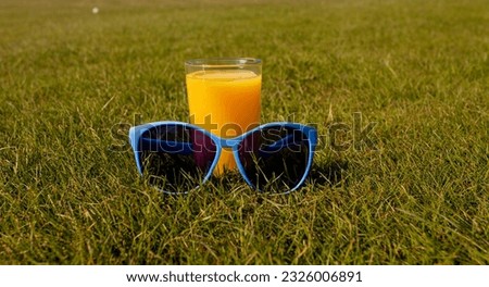 orange juice in a glass and sunglasses on a green lawn on a sunny day. holiday concept