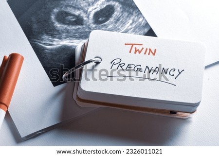 Flash card with the message Twin Pregnancy and ultrasound picture on desk. Close-up image, increasing twin birth rate concept. 