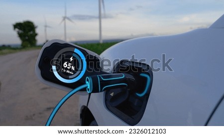 Electric car recharging energy from EV charging station display futuristic smart battery status hologram by EV charger plug cable in wind turbine farm. Alternative clean energy sustainability. Peruse
