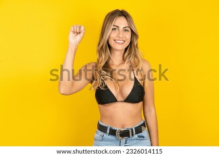 Young blonde woman on vacation wearing bikini over yellow background pointing up with fingers number ten in Chinese sign language Shi