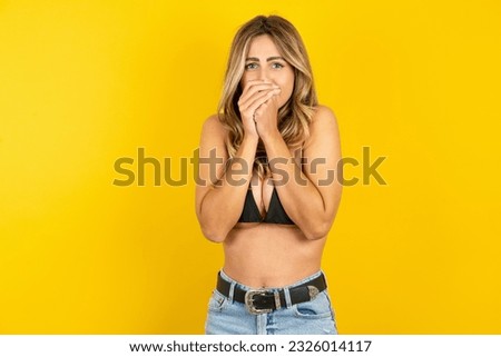Young blonde woman on vacation wearing bikini over yellow background holding oneself, feels very cold outside, hopes that will not get cold