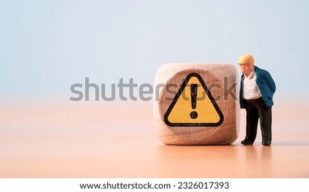Miniature figure of senior engineer standing and see at warning exclamation caution sign for notification maintenance and dangerous sign area and safety first concept.
