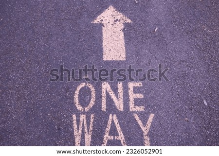 One Way sign and arrow painted on asphalt surface