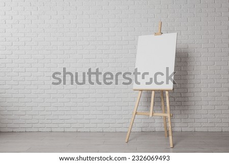 Wooden easel with blank canvas near white brick wall indoors. Space for text Royalty-Free Stock Photo #2326069493