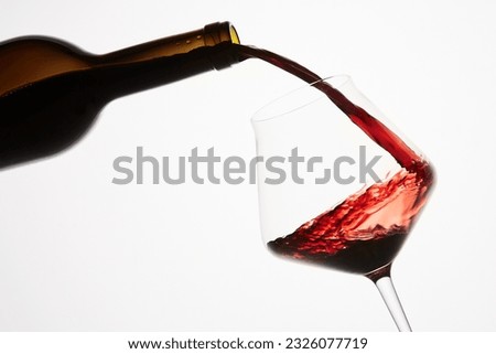 Red wine pouring into tilted wineglass from bottle. Royalty-Free Stock Photo #2326077719