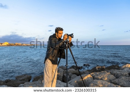 Beautiful photographer in leather and jeans makes photo video on camera for film, elegantly dressed, photographer, outdoor portrait, close up, brutal, tattoo, sunset in travel  
