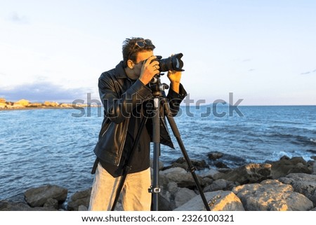 Beautiful photographer in leather and jeans makes photo video on camera for film, elegantly dressed, photographer, outdoor portrait, close up, brutal, tattoo, sunset in travel  