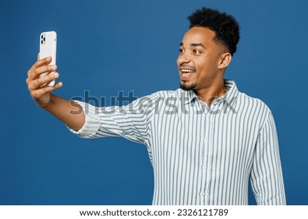 Young man of African American ethnicity he wear casual clothes shirt do selfie shot on mobile cell phone post photo on social network isolated on plain dark royal navy blue background studio portrait