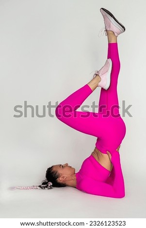 Sporty young woman doing stretching exercises in tracksuit isolated on pink background. Concept of healthy life and natural balance between body and mental development. Full length