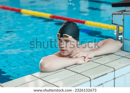 Fit strong swimmer with a black swimming cap looking at the pool, deep focusing on the race with swimming goggles. Royalty-Free Stock Photo #2326132673