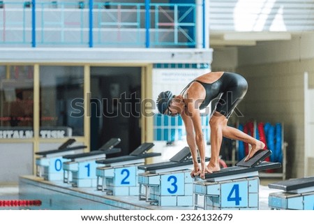 Elite female swimmer taking a position on the start block, using slingshot technique with a back footplate. Professional sport concept. Royalty-Free Stock Photo #2326132679